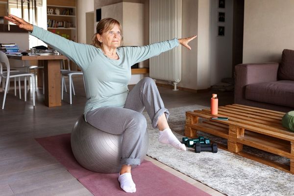 Older woman doing balance exercises on an exercise ball at home