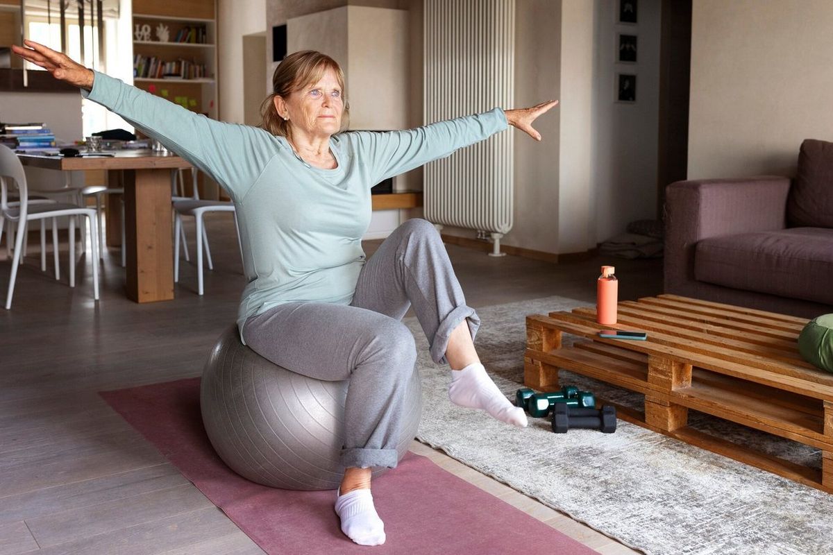 Older woman doing balance exercises on an exercise ball at home