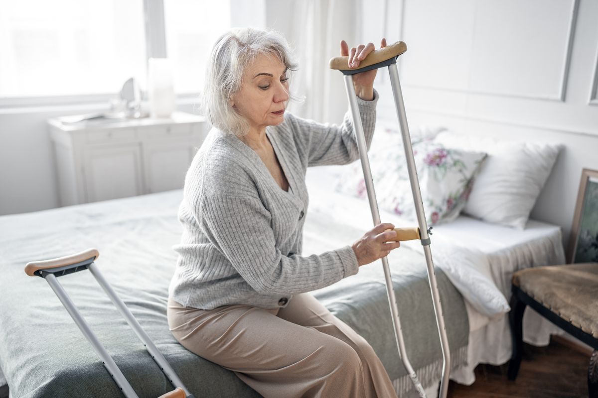 Older woman standing up with crutches at home