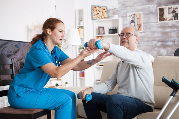 Physiotherapist helping an older man with arm exercises at home